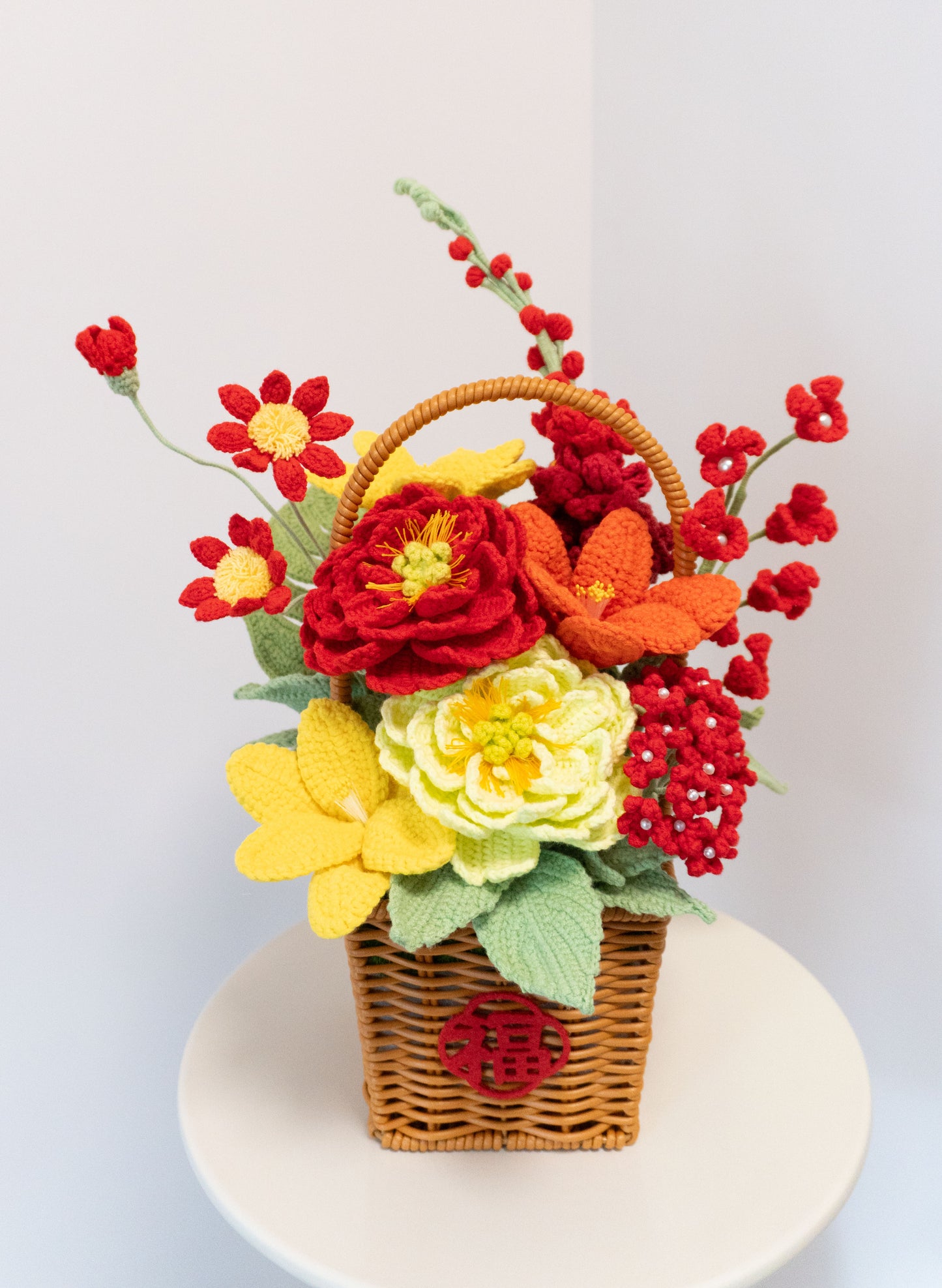 2026新春賀年編織花籃,手工針織紅色牡丹、黃色水仙、橙色花朵及紅色梅花,搭配綠色葉片與藤編花籃,籃身飾有紅色「福」字,喜慶鮮豔,適合新年送禮與家居擺設。