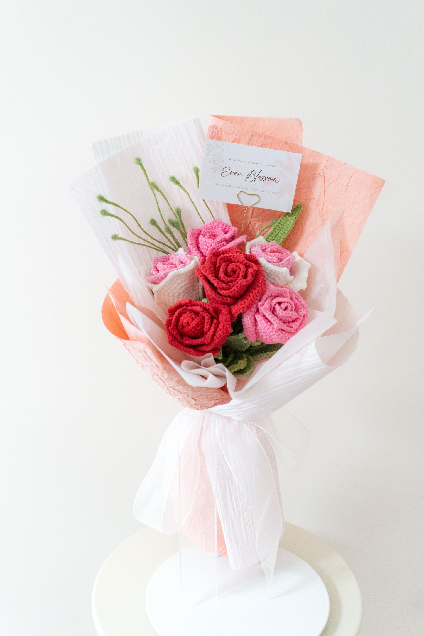 這是一束精緻的手工編織6枝裝混色玫瑰花束,採用紅、藍、紫、粉、橙等多種顏色可選,展現繽紛與浪漫的視覺效果。花束以白色與粉色包裝紙包裹,搭配綠色葉片和細緻的蝴蝶結裝飾,附帶「Ever Blossom」品牌標籤,充滿溫馨氣息。適合用作朋友生日、情人節或閨蜜聚會的理想禮物,設計獨特,極具紀念價值。