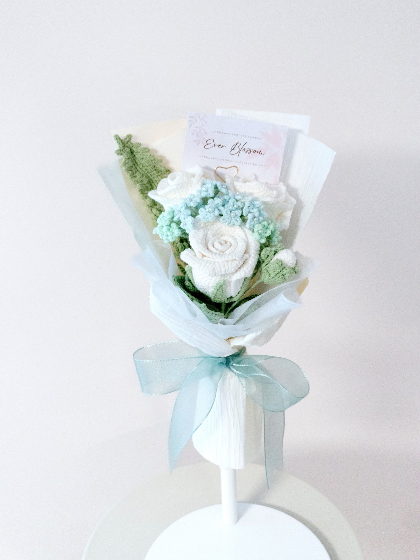 這款永恆小禮物為手工編織的玫瑰花束,包含白色與淡藍色玫瑰,搭配綠葉與薄紗包裝,綁上精緻藍色緞帶,展現溫柔浪漫風格。適合作為母親節送給母親的貼心禮物,或情人節/生日時贈予愛人的特別驚喜。花束永不凋謝,象徵永恆的情感,附贈「Ever Blossom」卡片增添個人化祝福,是手工愛好者與追求獨特小禮物的理想選擇,展現匠心獨具的細膩設計。
