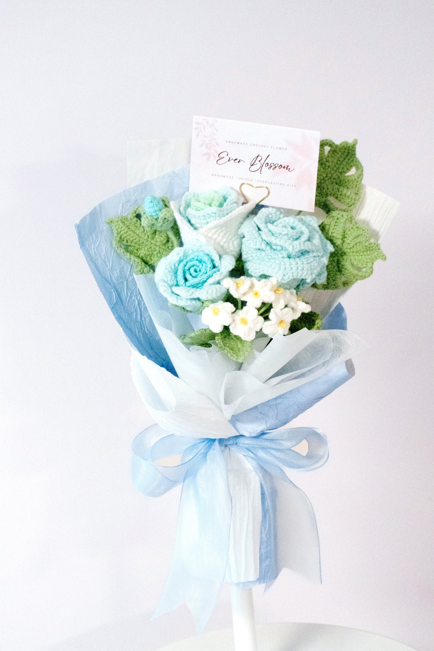 這是一束精緻的手工編織3枝裝混色玫瑰勿忘我花束,採用粉藍和粉紅兩色可選,展現柔和浪漫的氣息。花束以藍色薄膜包裝,搭配綠色葉片和白色勿忘我點綴,附帶「Ever Blossom」品牌標籤,綁以藍色蝴蝶結增添優雅感。適合用作情人節、生日或表達心意的禮物,設計細膩,充滿溫暖與創意。