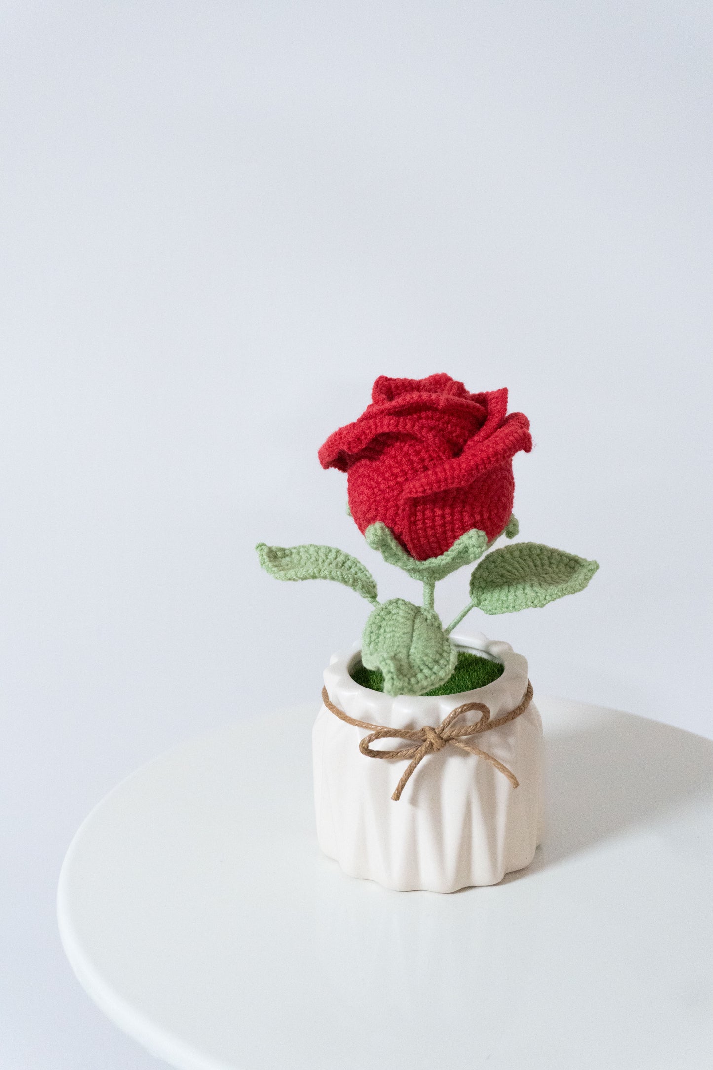 這款手工編織紅玫瑰擺設以鮮紅花瓣與綠葉設計,置於白色陶瓷花瓶中,繫上麻繩增添自然風格,適合用作辦公室桌面或居家室內裝飾。永不凋謝的花卉象徵熱情與永恆,完美契合職場人士提升工作環境,或家居愛好者增添溫馨氛圍,展現手工工藝的精緻與實用價值。